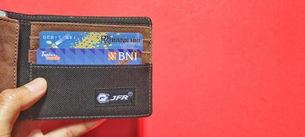 Man holding wallet containing credit card and bank savings card in Indonesia, isolated against background and negative space. photo