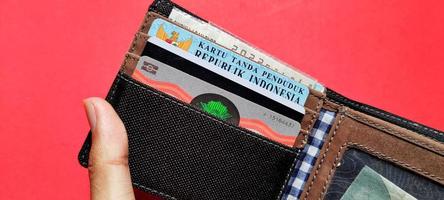 Man holding a wallet containing identity cards, driving licenses and motor vehicle certificates, isolated on red background. photo