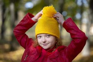 niña en un amarillo de punto sombrero en otoño. retrato de un niño en el otoño parque. foto