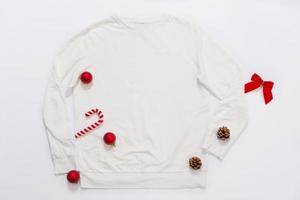 Close up white blank template sweatshirt copy space. Christmas Holiday concept. Top view mockup sweatshirt. Red holidays decorations on white background. Happy New Year accessories. Xmas outfit photo