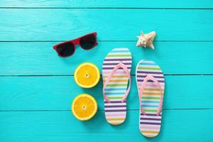 flip flops, red sunglasses, shell and orange fruit on blue wooden background. Top view and summer time.