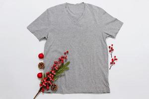 Close up grey blank template t shirt with copy space and Christmas Holiday concept. Top view mockup t-shirt and red holidays decorations on white background. Happy New Year accessories. Xmas outfit photo