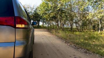 Rear side of traveling  car on soil road with turn on turn light signal. Dirt road with trees and grass and a sharp curve in front. photo