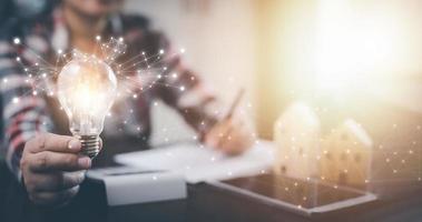 Businesswoman hand holding light bulb with icons and working on the desk, Creativity and innovation are keys to success.Concept of new idea and innovation with energy and power , working at home, photo
