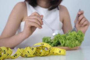 asiático mujer son cansado de comiendo vegetales utilizando un tenedor de lechuga en el plato. sano comida y dieta concepto foto