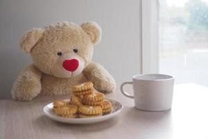Teddy bear sit drinking cocoa and cookies on the table. photo