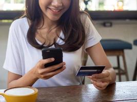A woman sitting in a coffee shop, using a phone, transferring money, shopping with a credit card through an app, via a notebook, convenient and quick options photo