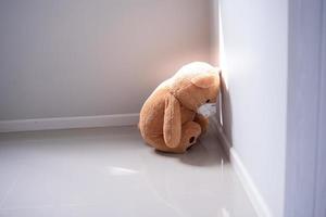 concepto infantil de tristeza. oso de peluche con máscara sentado solo contra la pared de la casa, se ve triste y decepcionado. foto