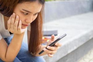 Adolescente muchachas sentar y Mira a el teléfono retenida en su manos, tristemente esperando para su del novio llamada o mensaje. foto