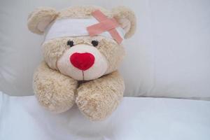 Teddy bear with a wound dress, wound and broken hands. Sleeping in bed. Sickness of children photo