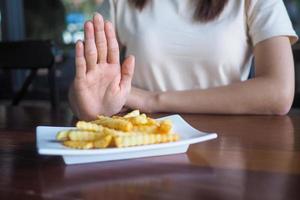 cuidado de la salud mujer empujar el platos dentro francés papas fritas hacer no comer frito y Rica en grasas comidas foto