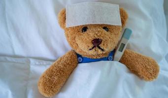 Brown teddy bear with fever reducing sheet and body temperature monitor. Used for health insurance or illness concepts photo