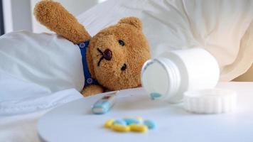 The sad teddy bear had a headache and fever, lying ill in the bed. photo