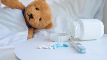 Brown teddy bear is sick in bed depression beside, there was a medicine placed on the table. photo