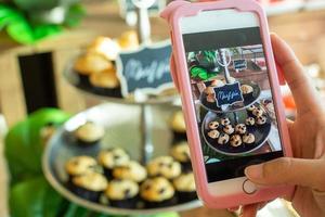 The cafe owner uses a smartphone to take pictures of newly finished cupcakes to promote on online media and websites. Selling products online photo