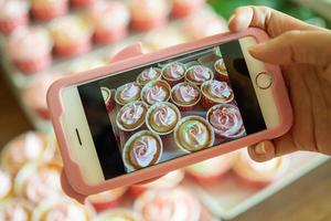 The cafe owner uses a smartphone to take pictures of newly finished cupcakes to promote on online media and websites. Selling products online photo