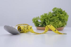 lechuga y cinta métrica envuelta alrededor de una cuchara y un tenedor. concepto de alimentación y dieta saludable foto