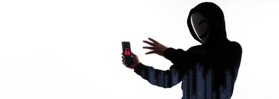 Hacker Anonymous and face mask with smartphone in hand. Man in black hood shirt holding and using mobile phone on white background. Represent cyber crime data hacking or stealing personal data concept photo