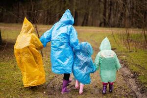 Rear view of mother and three children walking in the forest after rain in raincoats together. photo