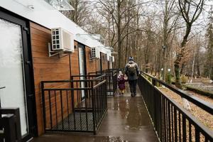 Back of father with daughters walking on terrace of one-storey modular houses in spring rainy forest. photo