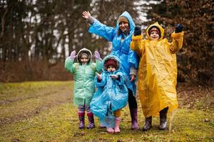 madre y Tres niños en el bosque después lluvia en impermeables juntos. foto