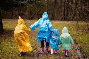 Rear view of mother and three children walking in the forest after rain in raincoats together. photo