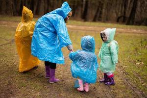 Rear view of mother and three children walking in the forest after rain in raincoats together. photo