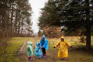 Mother and children walking in the forest after rain in raincoats together. photo