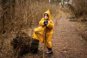 chico en amarillo impermeable con Iniciar sesión a manos cerca tocón en el bosque después lluvia. foto