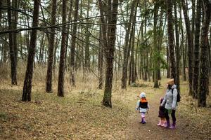 Mother and two daughters with backpacks walking along the forest road together. photo