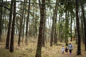 Mother and two daughters with backpacks walking along the forest road together. photo
