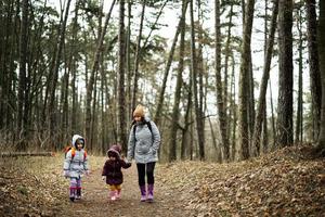 madre y dos hijas con mochilas caminando a lo largo el bosque la carretera juntos. foto