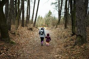 Back of mom with backpack and daughter walking along the forest after rain together. photo