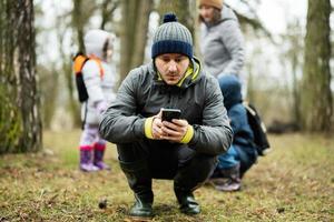 hombre se sentó abajo a Mira a el teléfono en el bosque con sorprendido rostro. foto