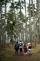 Back of mom and children with backpacks walking along the forest road after rain together. photo