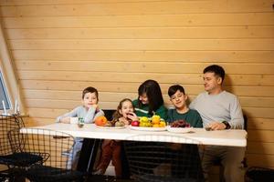 familia con Tres niños comer frutas en de madera país casa en fin de semana. foto