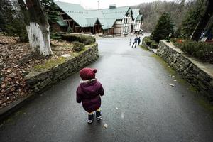 Back of baby girl walking on path near wooden cottage in the forest. Country house. photo