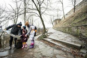 Family tourist look at map with three children, stand on wet path to an ancient medieval castle fortress in rain. photo