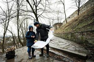 padre y hijo turista Mira a mapa, estar en mojado camino a un antiguo medieval castillo fortaleza en lluvia. foto