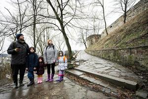 Family tourist with three children stand on wet path to an ancient medieval castle fortress in rain. photo