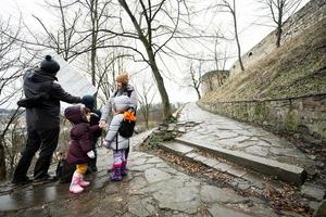 Family tourist look at map with three children, stand on wet path to an ancient medieval castle fortress in rain. photo