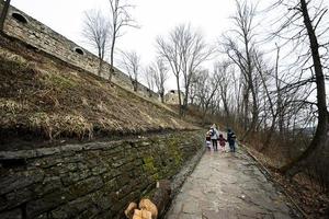 Back of mother and children walk up the wet path to an ancient medieval castle fortress in rain. photo