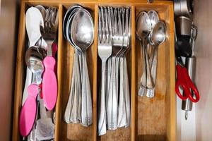 Clean and silver spoons, forks at kitchen drawer with cutlery set. Flat lay view of organizer tray with simple kit of utensils in open storage box. photo