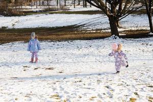 Two sisters in winter snowsuit playing together in sunny day. photo