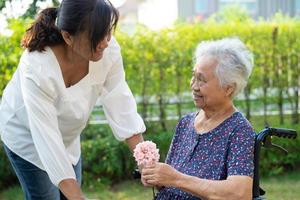 Caregive talk and help Asian elderly woman holding flower, smile and happy in the sunny garden. photo