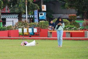 Kudus, December 2022. Photograph of visitors sitting relaxed enjoying the afternoon on the grass of the Kudus city square. photo