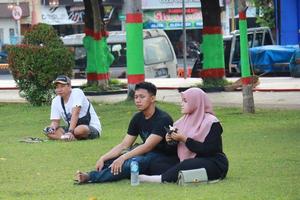 Kudus, December 2022. Photograph of visitors sitting relaxed enjoying the afternoon on the grass of the Kudus city square. photo