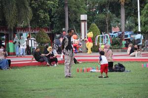 Kudus, December 2022. Photograph of visitors sitting relaxed enjoying the afternoon on the grass of the Kudus city square. photo