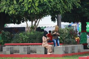 Kudus, December 2022. Photograph of visitors sitting relaxed enjoying the afternoon on the grass of the Kudus city square. photo