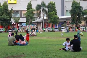 Kudus, December 2022. Photograph of visitors sitting relaxed enjoying the afternoon on the grass of the Kudus city square. photo